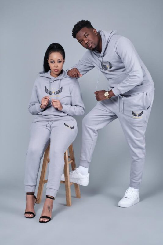 A man and woman posing for a photo in a grey hoodie and sweatpants.